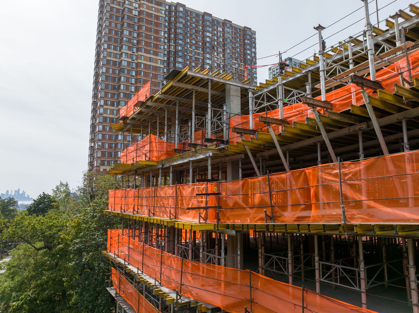 ULMA formwork and orange safety screens wrapping the upper floors of a high-rise under construction, city skyline beyond
