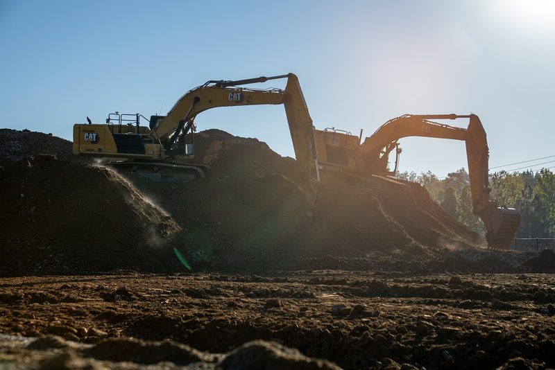 Two CAT excavators working the pad backlit, dust hanging in the light
