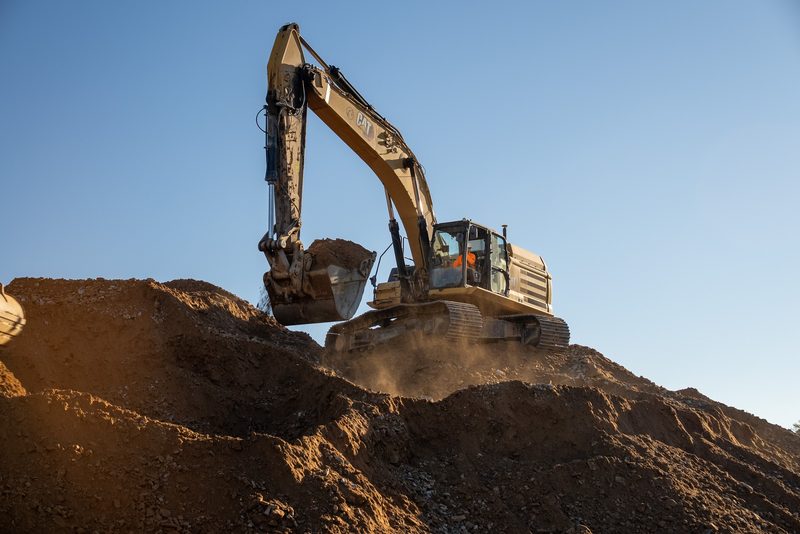 A CAT excavator swinging a full bucket over the stockpile