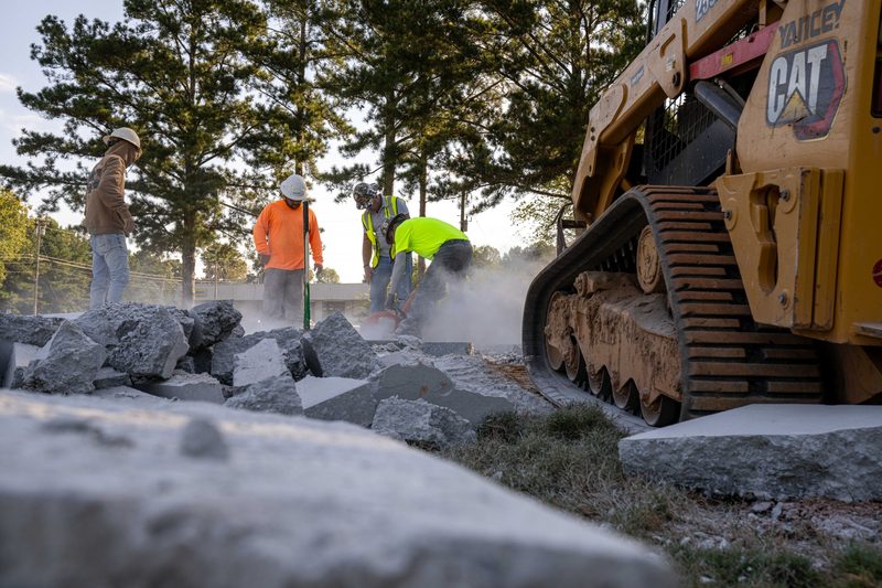 A CAT track loader working the rock, crew clearing behind it