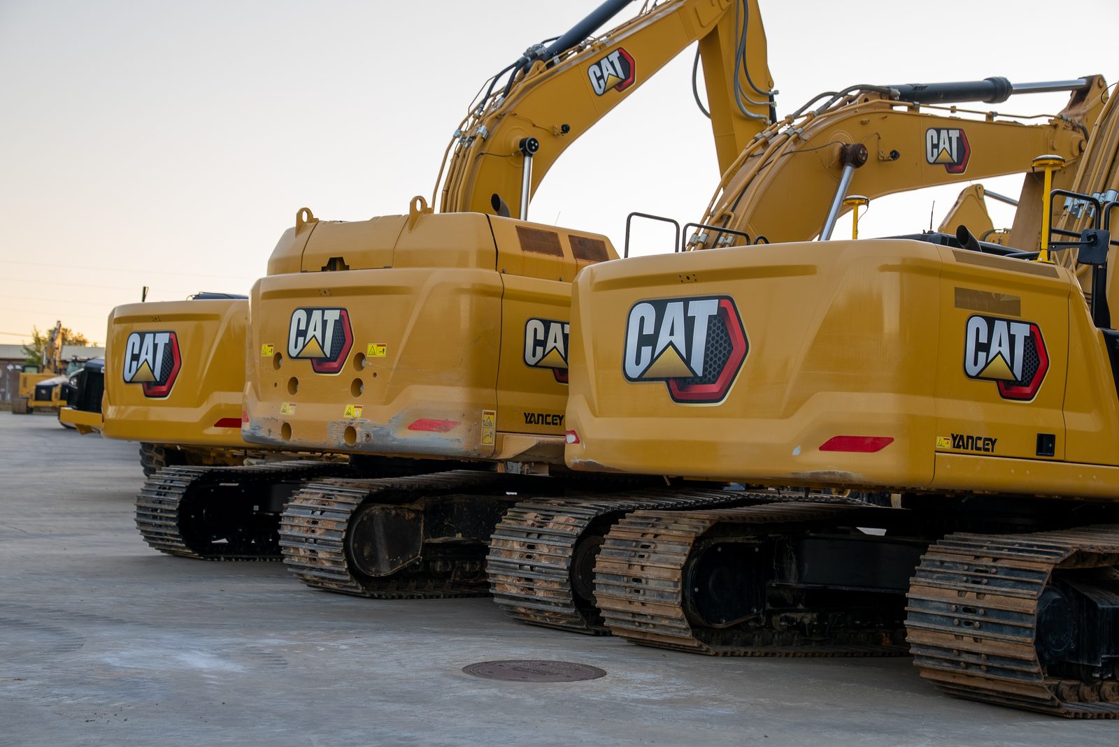 A row of CAT excavators lined up nose to tail on the Yancey Bros. Co. lot, counterweights facing the camera