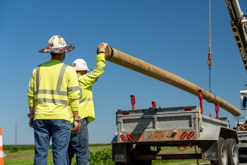 Two linemen steadying a pole as the derrick takes its weight