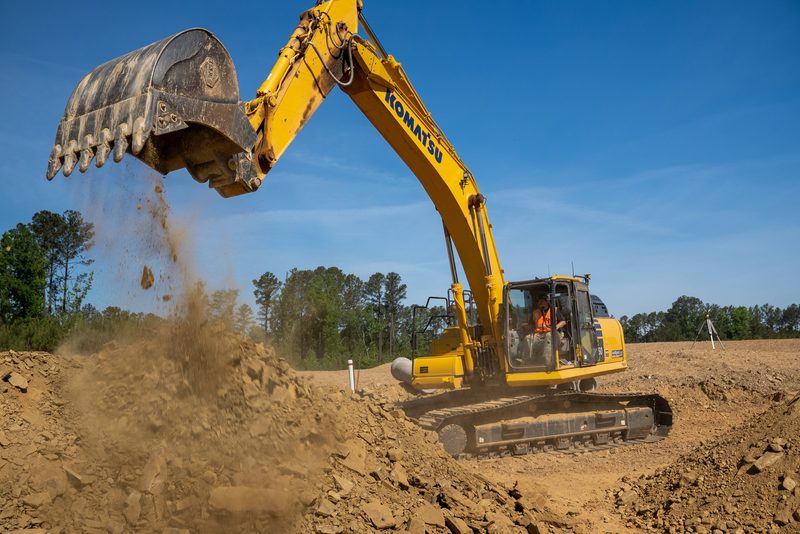 An excavator swinging a full bucket, dirt spilling over the lip