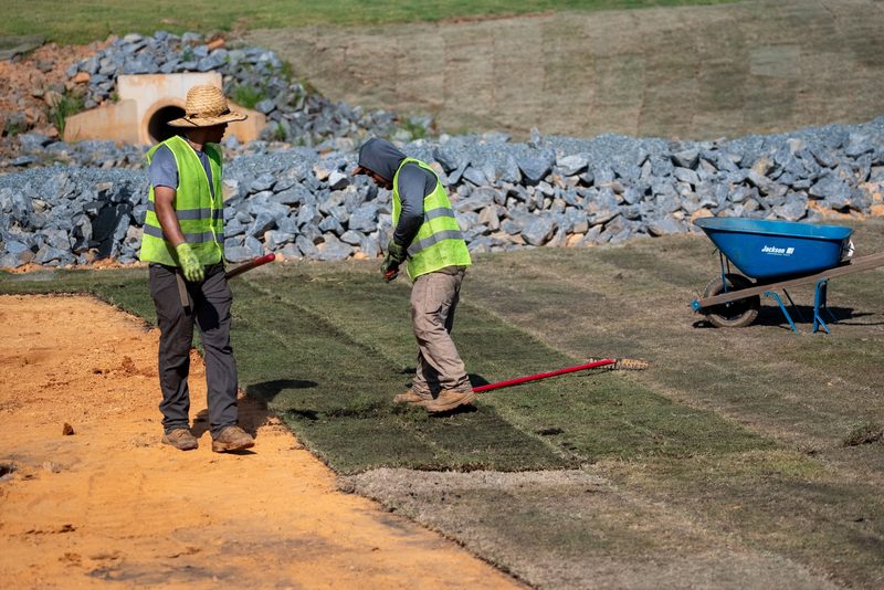 Two workers raking freshly laid sod on the slope above the riprap