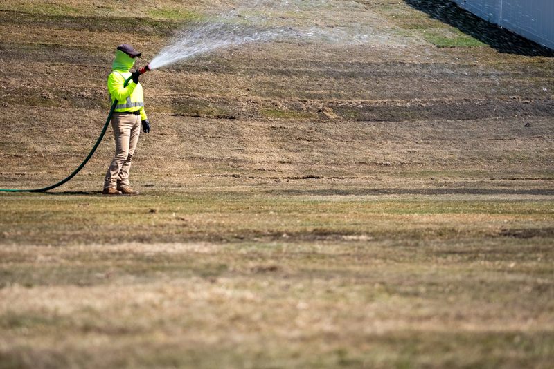 A worker arcing a fan of water across a freshly seeded slope