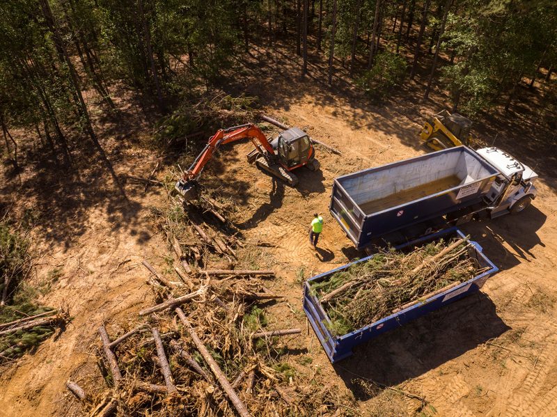 Aerial on the grapple swinging brush into a roll-off container