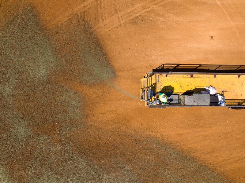 Top-down on the hydroseeding rig, green slurry spreading across red clay